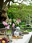 Büste, Steinvase mit Blumen, Vogelkäfig und Obstteller auf einem Tisch im Garten
