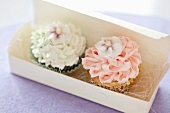 Two cupcakes topped with frosting in a gift box
