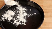 A greased quiche dish being sprinkled with flour