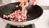 Diced bacon being added to a pan of clarified butter
