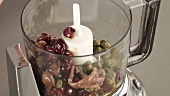 Olives, capers and sardine fillets being placed in a blender