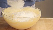 Sponge cake being made: flour being sieved into a beaten egg white and egg yolk mixture