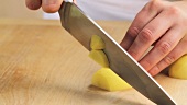 A peeled potato being halved and chopped