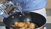 Unpeeled potatoes being placed in a pot and covered with water