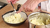 Mashed potatoes being placed on fish pie ingredients