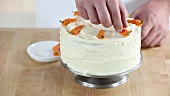 A carrot cake being decorated with marzipan carrots (USA)