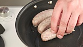 Oil being poured into a hot pan and sausages being fried