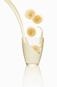 Bananenscheiben fallen in ein Milchglas