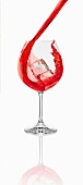 A red cocktail being poured into a glass with an ice cube