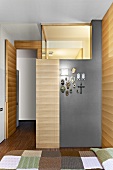 Modernes Schlafzimmer mit beleuchtetem Badeinbau und teilweise mit Holz verkleidet - Devotionalien an grau getönter Wand aufgehängt