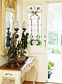 Table lamp made from antique sculptures on a console table in front of an entry door with colorful leaded glass panel