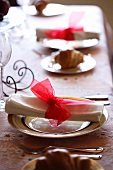 A Christmas place setting with a rolled napkin and a red chiffon bow