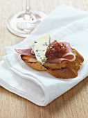 A slice of toasted baguette topped with raw ham, blue cheese and rhubarb chutney