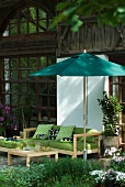 Comfortable terrace sofa with green cushions below parasol in front of rustic farmhouse