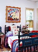 Antikes, blaues Landhausbett mit bunter Bettwäsche unter modernem Pop Art Gemälde