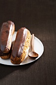 Two chocolate eclairs on a plate with a wooden spoon