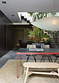 Simple wooden bench and retro, metal dining table below designer pendant lamp in open-plan interior
