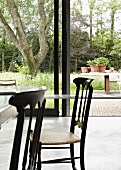 Dining table and Chiavari chairs in front of sliding glass doors leading to garden