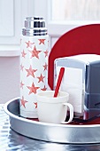 A Thermos flask decorated with stars, a spoon and a napkin dispenser on a tray