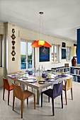 Place settings on modern dining table below pendant lamp with red lampshade in open-plan interior
