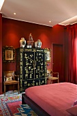 Red bedroom - modern double bed in front of Oriental-style black and gilt wardrobe against red wall