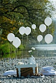 Sommerliches Picknick an einem Flussufer mit Tischchen aus einem Karton, weissen Bodenkissen und Luftballons
