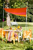 Farbenfrohes, selbstgenähtes Sonnensegel an weiss lackierten Bambusstäben über sommerlich gedecktem Tisch im Garten