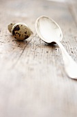 A quail's egg next to a silver spoon