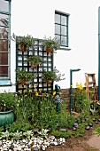 Blumenbeet mit Kieselsteinen und selbstgebautes Blumentopfgitter an der Hauswand