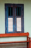 Sitzbank aus Mahagonyholz an Hauswand unter Fenster mit geschlossenen Läden aus Holz