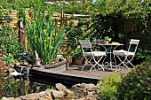 Corner of garden with creeper-covered wooden fence and table and chairs on wooden deck next to small pond