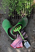 Still-life with gardening tool and gloves next to gardening clogs