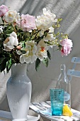 Summer bouquet in white ceramic vase next to retro-style drinking glass and bottle on garden chair