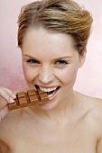 A woman grinning and biting into a piece of milk chocolate