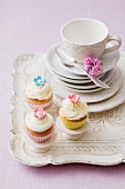 Three cupcakes with a stack of plates and a teacup