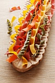 Various types of coloured tagliatelle in a wooden dish