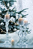 Kerzenhalter aus Glas mit brennenden Kerzen vor Tannenbaum