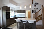 Traditional wooden staircase in open-plan, modern kitchen-dining room with bar stools at free-standing island