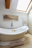 Soft beige and wood tones in white bathroom with free-standing bathtub below angled skylight