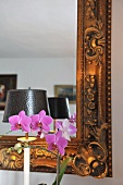 Lila blühende Orchidee vor Spiegel mit verziertem Goldrahmen