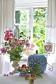 Weiß blau bemaltes Keramikgefäss mit Deckel und Blumenstrauss auf dem Tisch vor Fenster mit Gartenblick