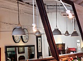 Pendant lamps with metal lampshades and clocks on wall of restaurant interior reflected in two large wall mirrors