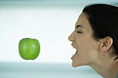 Junge Frau will einen grünen Apfel mit dem Mund auffangen
