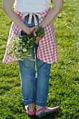 Frau im Garten hält Blumenstrauß hinter ihrem Rücken