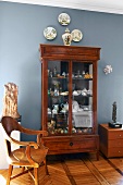 Chinese vase, decorative wall plates and collection of china in antique display cabinet against wall painted light blue