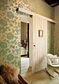 Classic rocking chair against elegant floral wallpaper and half-open sliding door showing view of bedroom beyond