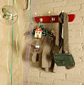 Kinderkleidung und Tasche auf Retro Wandhakenleiste an getünchter Ziegelwand montiert