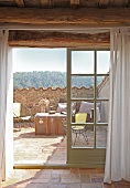 View through French windows onto Mediterranean roof terrace with wire furniture and travelling trunk used as table