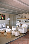 Helle Polstermöbel auf Rollen und Holzhocker als Beistelltische in mediterranem Wohnzimmer mit Rippendecke und Terracottafliesen