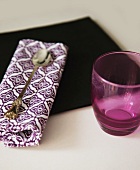 Purple drinking glass next to silver spoon on patterned linen napkin